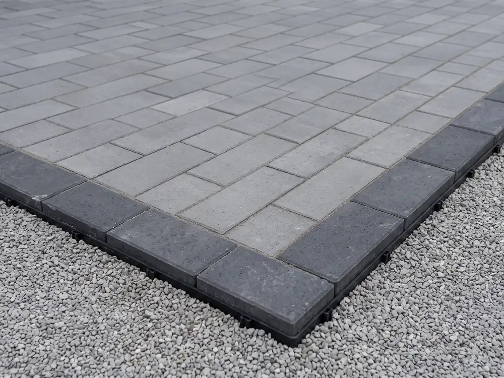 Gray paver edge with a charcoal border row and a black edge restraint beside gravel
